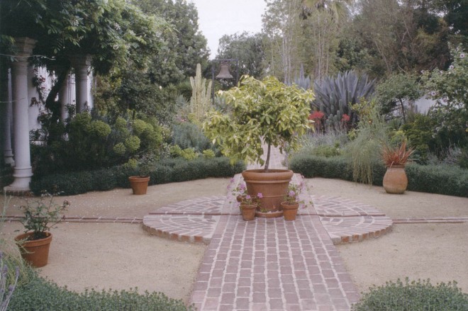 A remnant of the original brick pathway passes through the mediterranean garden that fills the space between the pergola (on the left) and the wall at the property line (on the right); the rill crosses through the brick path, connecting the fountain on the house with a new fountain on the perimeter wall