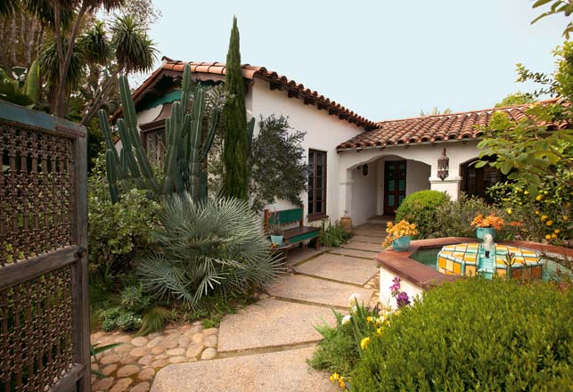 The mature front courtyard offers visitors colorful foliage, contrasting textures, and a congenial inviting pathway framed by blooming freesias, and an espaliered ceanothus flushed with violet blue blooms. Photo: Jeff Dunas.